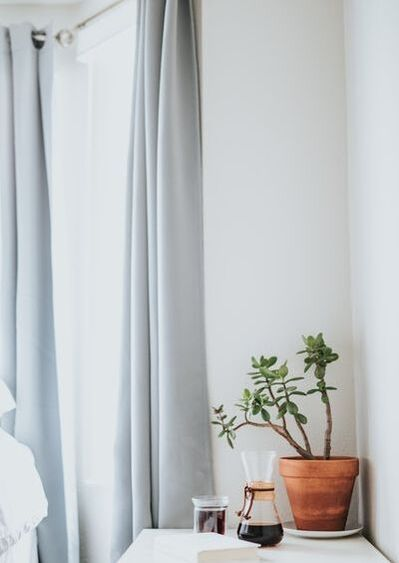 Tall grey drapes hang on the side of an apartment window with a small table and green succulent plant next to it.